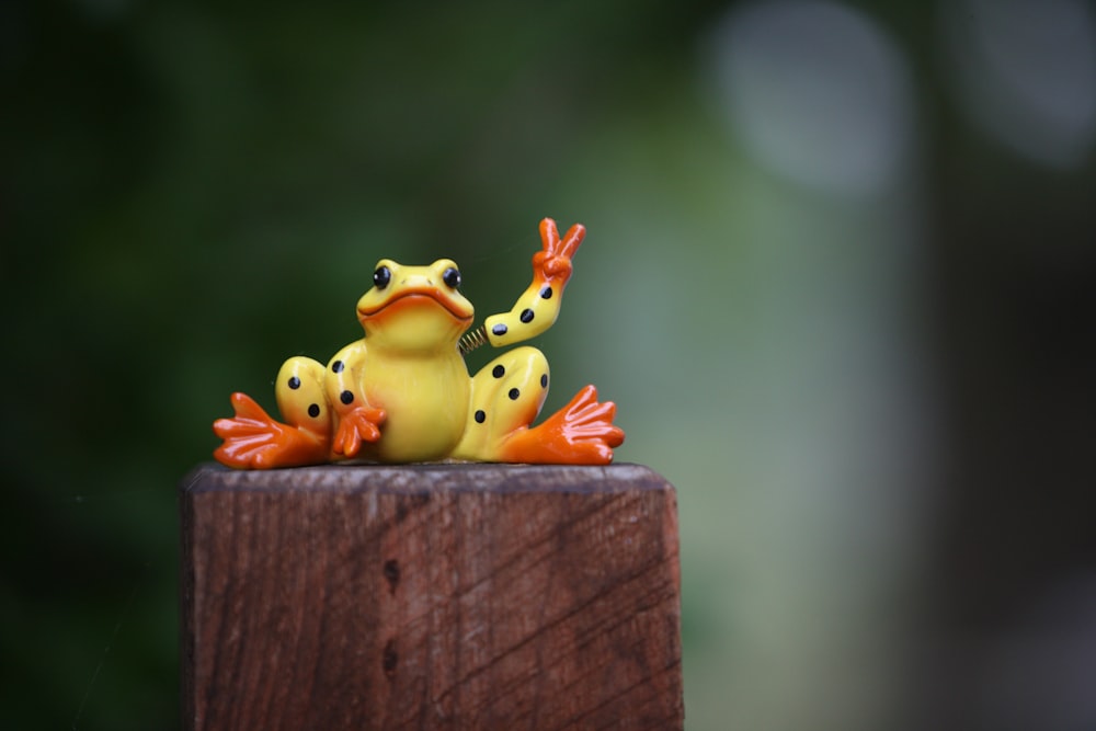 a yellow frog sitting on top of a wooden post