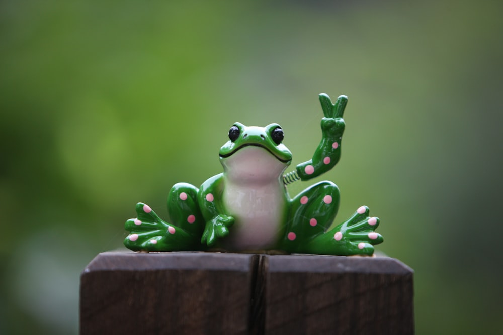 a green frog sitting on top of a wooden fence