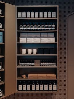 A well-organized shelf displaying a variety of products, including bottles and boxes, neatly arranged. The products appear to be skincare or personal care items, and the packaging is minimalist with neutral tones. Ceramic cups are also visible among the items on the shelf, adding a touch of elegance.