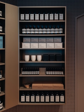 A well-organized shelf displaying a variety of products, including bottles and boxes, neatly arranged. The products appear to be skincare or personal care items, and the packaging is minimalist with neutral tones. Ceramic cups are also visible among the items on the shelf, adding a touch of elegance.