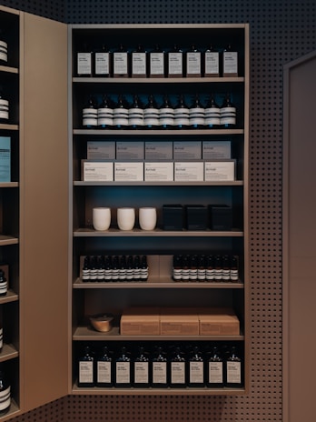 A well-organized shelf displaying a variety of products, including bottles and boxes, neatly arranged. The products appear to be skincare or personal care items, and the packaging is minimalist with neutral tones. Ceramic cups are also visible among the items on the shelf, adding a touch of elegance.