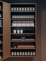 A well-organized shelf displaying a variety of products, including bottles and boxes, neatly arranged. The products appear to be skincare or personal care items, and the packaging is minimalist with neutral tones. Ceramic cups are also visible among the items on the shelf, adding a touch of elegance.