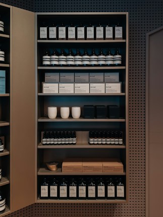 A well-organized shelf displaying a variety of products, including bottles and boxes, neatly arranged. The products appear to be skincare or personal care items, and the packaging is minimalist with neutral tones. Ceramic cups are also visible among the items on the shelf, adding a touch of elegance.