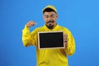 A smiling teacher recording a video lesson with a whiteboard in the background.