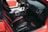 The interior of a car featuring black and red leather seats, a detailed dashboard with a steering wheel, a gear shift, and a center console with cup holders. The door trim and floor mat are also visible, with the mat displaying the words 'CHARGER SRT'. Another red car is partially visible through the window.