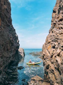 A kayaker paddling near towering cliffs under a clear blue sky.