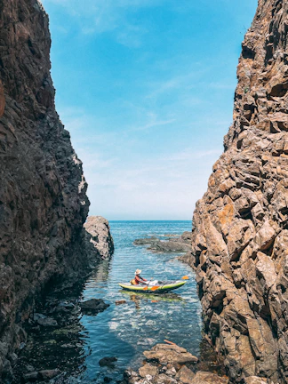 A kayaker paddling near towering cliffs under a clear blue sky.
