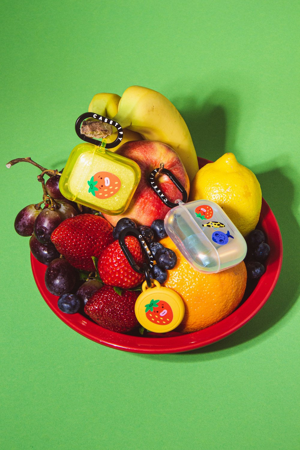 a red bowl filled with assorted fruit on top of a green table