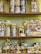 A variety of neatly arranged nut gift packages are displayed on shelves. Each package is wrapped with golden and purple ribbons and labeled with 'Pistacherie'. Different types of nuts and nut mixes can be seen, including pistachios.