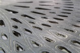 Intricate metal surface with cut-out teardrop-shaped patterns, showcasing a blend of light and shadow across the textured material.