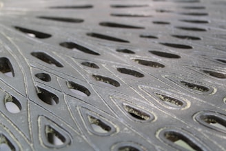 Intricate metal surface with cut-out teardrop-shaped patterns, showcasing a blend of light and shadow across the textured material.