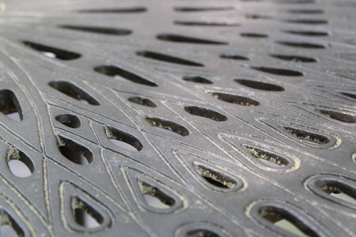 Intricate metal surface with cut-out teardrop-shaped patterns, showcasing a blend of light and shadow across the textured material.
