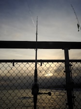 A well-worn fishing rod leaning against a wooden dock at sunrise.