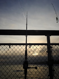 A well-worn fishing rod leaning against a wooden dock at sunrise.