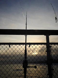 A rugged fishing rod resting against a weathered wooden dock at sunrise.