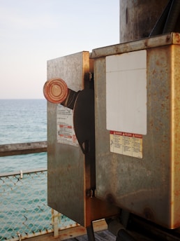 a close up of a rusted metal box near a body of water