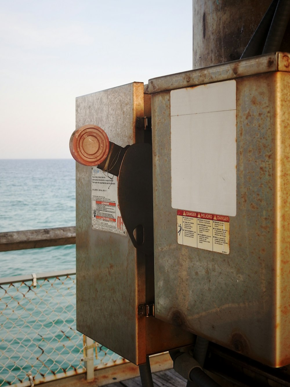 Un primer plano de una caja de metal oxidada cerca de un cuerpo de agua