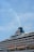 A large cruise ship with multiple decks and lifeboats visible, adorned with flags and a smokestack emitting a thin stream of smoke against a clear blue sky.