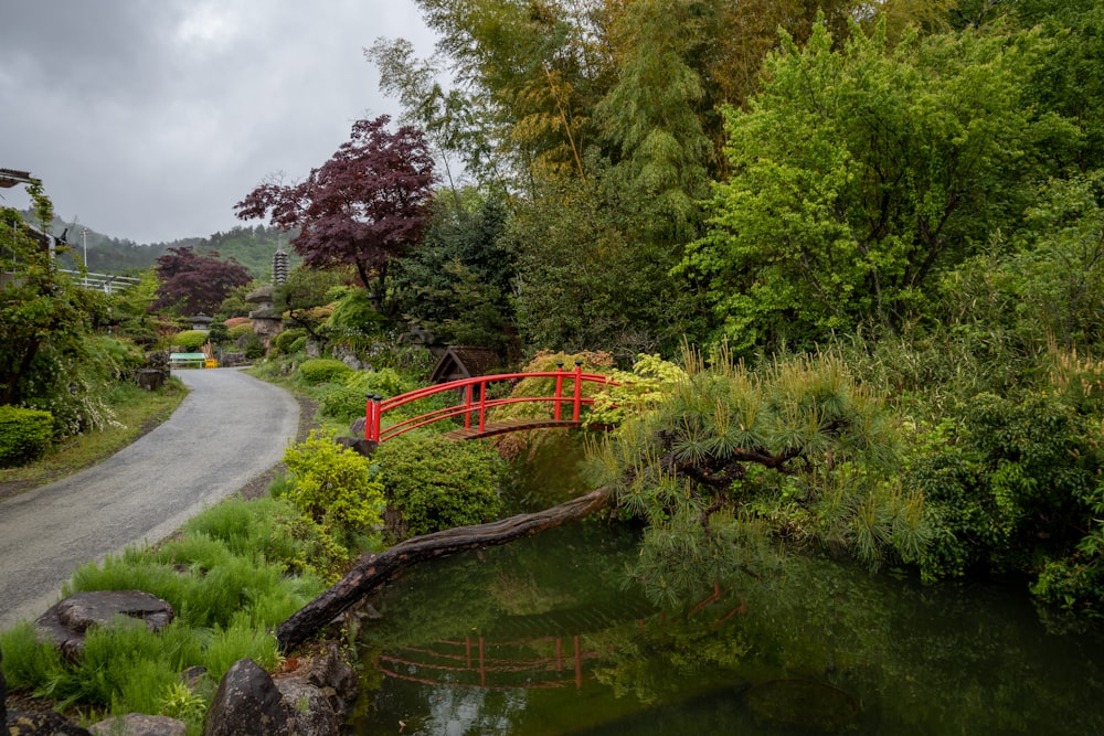 a red bridge over a small pond in a park