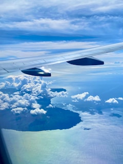 An aerial shot of a plane flying over a sparkling blue ocean near a tropical island.
