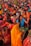 A vibrant gathering of people, predominantly women, dressed in colorful traditional attire, participating in a cultural or religious event. Many are holding offerings or ceremonial items such as fruits and flowers. The crowd is dense, with individuals and groups engaged in various activities, creating an atmosphere of festivity and devotion.