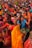 A vibrant gathering of people, predominantly women, dressed in colorful traditional attire, participating in a cultural or religious event. Many are holding offerings or ceremonial items such as fruits and flowers. The crowd is dense, with individuals and groups engaged in various activities, creating an atmosphere of festivity and devotion.