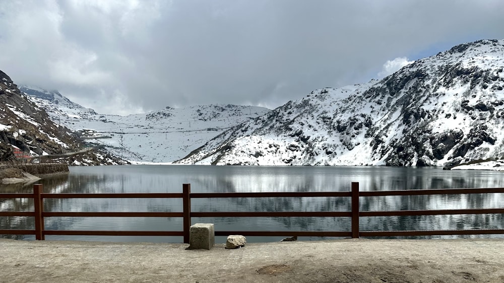 a lake surrounded by snow covered mountains and a wooden fence