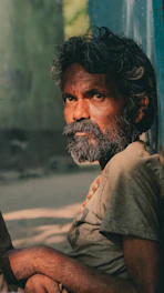 Tony standing against a weathered adobe wall, his white beard catching the warm desert light, eyes steady and voice ready to tell a story.