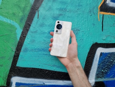 An urban youth holding a phone with a custom skin from phonevibee.com, standing against a graffiti wall that matches the brand’s neon orange and navy color palette.