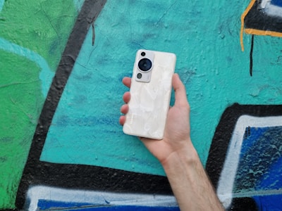 Hands holding a slim mobile with a minimalist design against an urban graffiti wall.