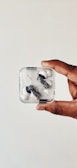A hand holding a transparent case containing a pair of wireless earbuds with a minimalist design.