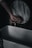 A hand is poised below a rustic, circular washbasin faucet, which is releasing a thin stream of water. The scene has a dimly lit, moody atmosphere.