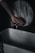 A hand is poised below a rustic, circular washbasin faucet, which is releasing a thin stream of water. The scene has a dimly lit, moody atmosphere.