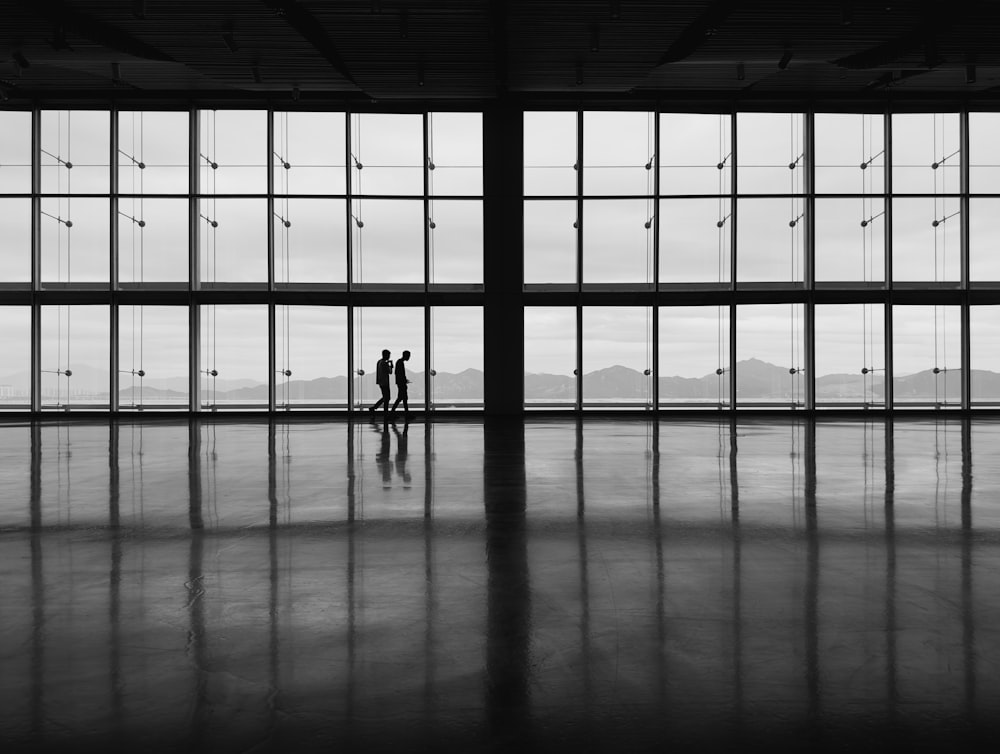 uma foto em preto e branco de duas pessoas em frente a grandes janelas