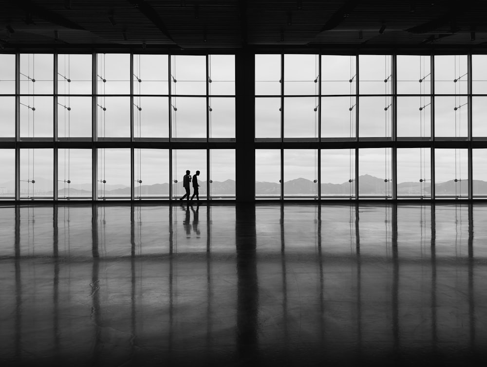 a black and white photo of two people standing in front of large windows