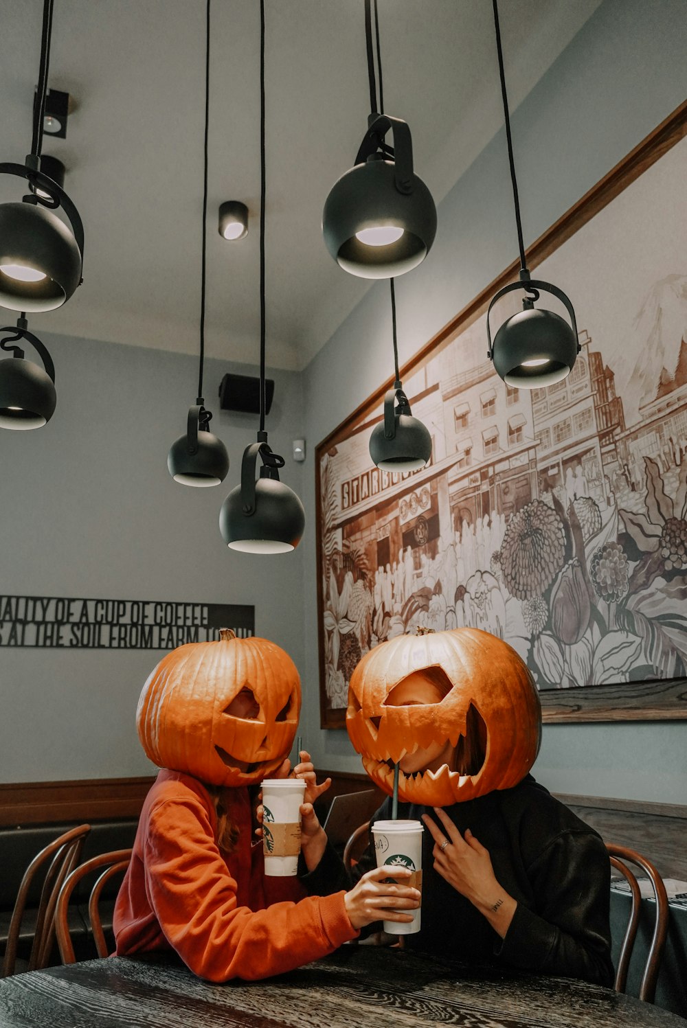 two people sitting at a table with pumpkin heads on their heads