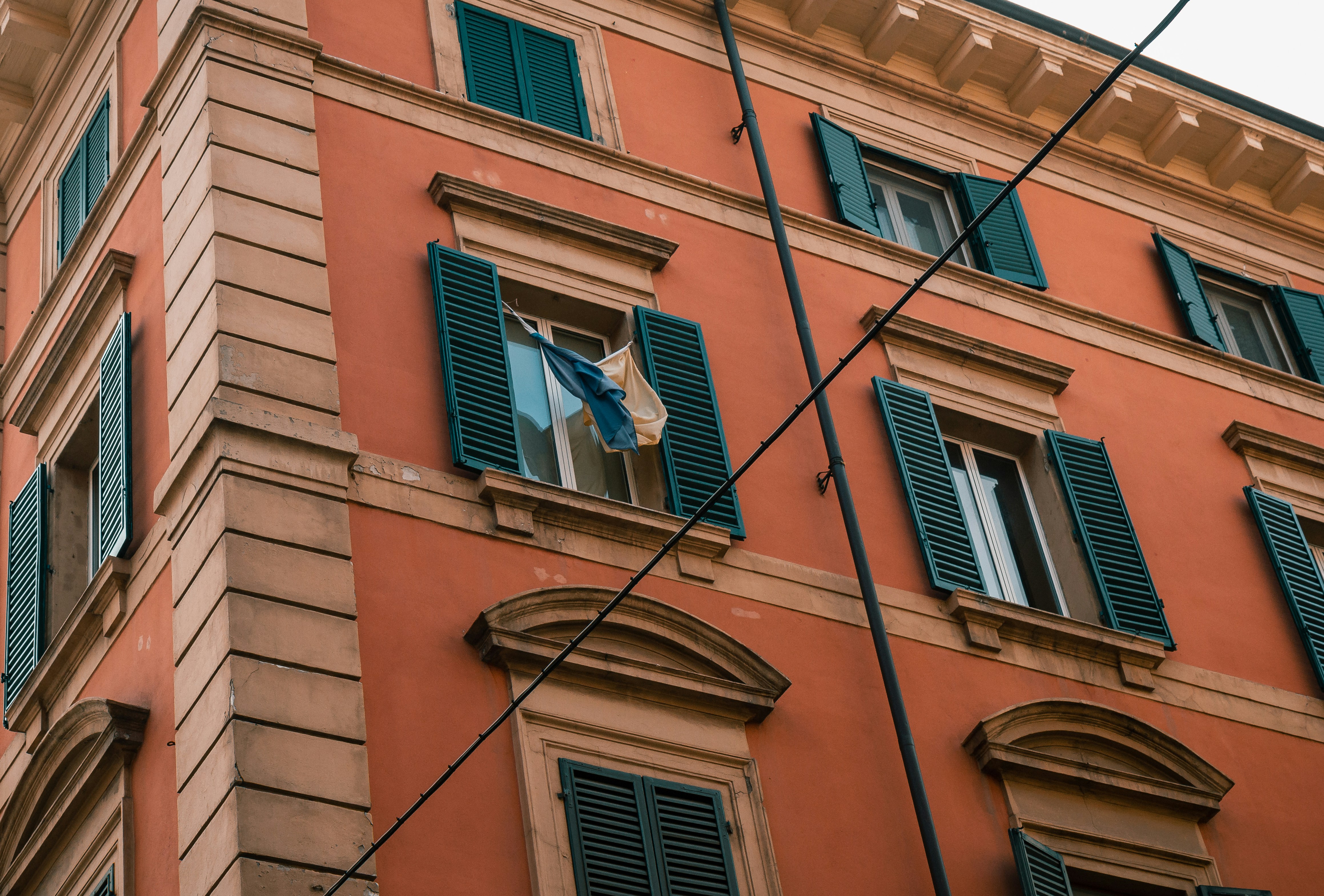 an orange building with green shutters and a flag hanging from the window, Windows
