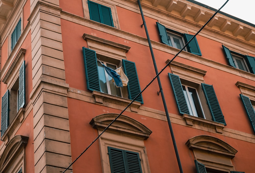 an orange building with green shutters and a flag hanging from the window