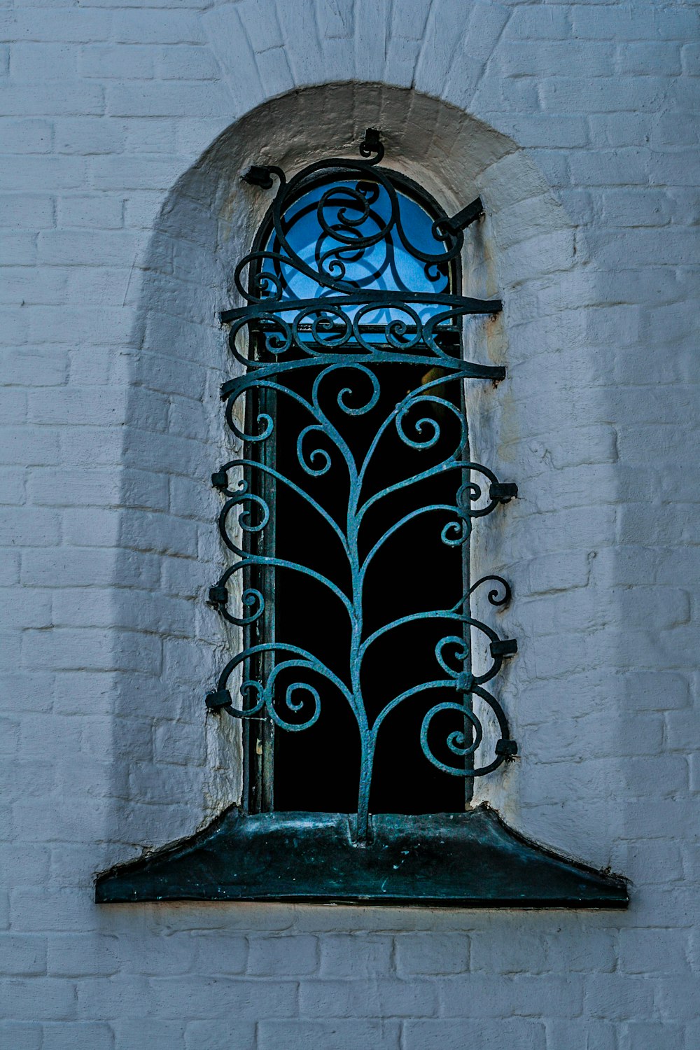 a window on a white brick wall with iron bars