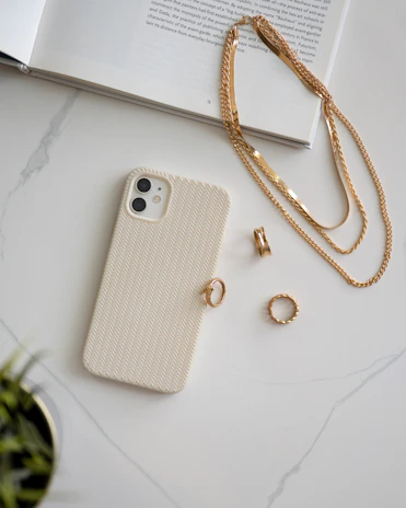Arrangement of minimalist gold jewelry pieces beside a sleek tech gadget on a marble surface.