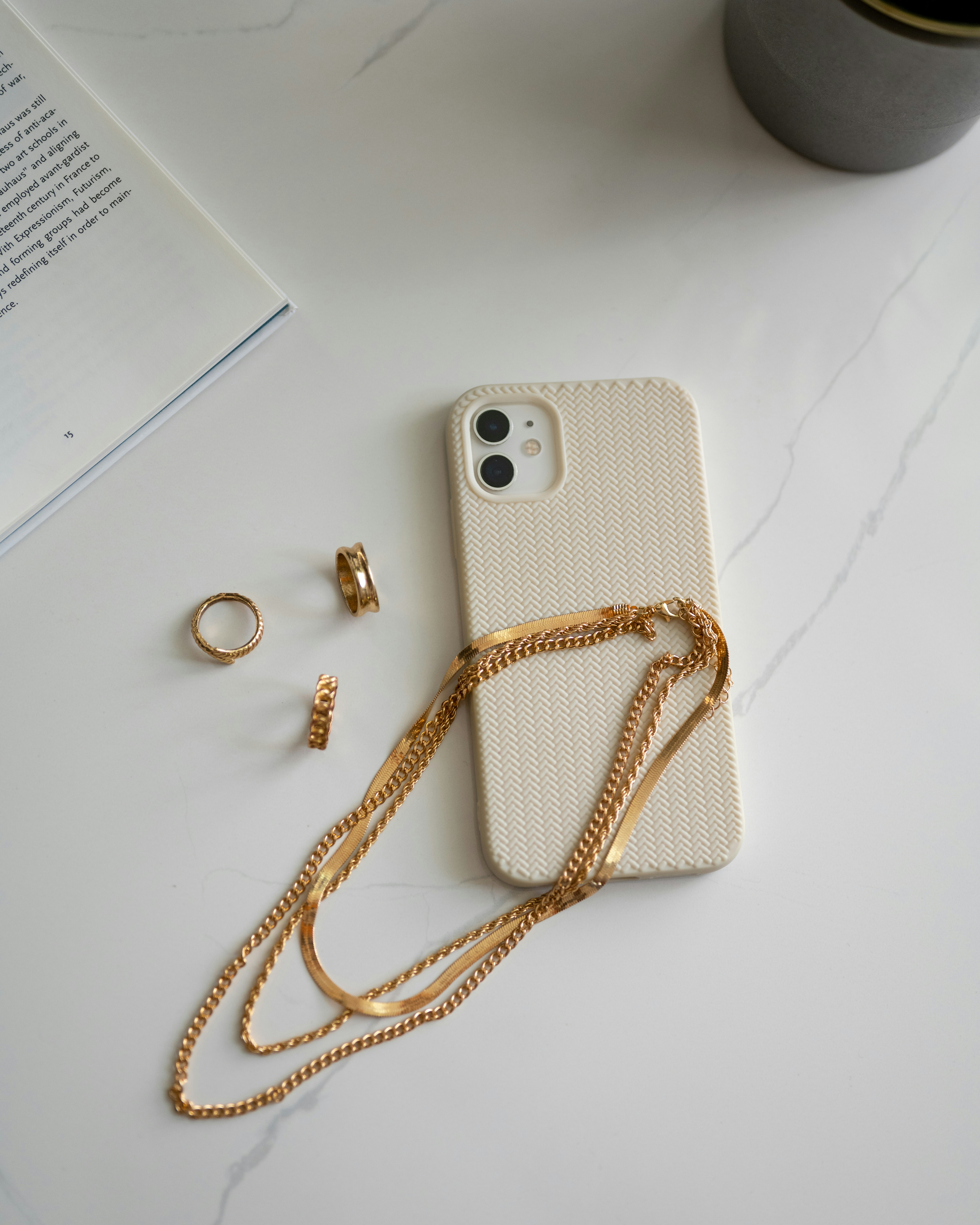 Fine jewelry accessories — delicate gold necklaces and rings arranged on a white marble surface in bright natural daylight