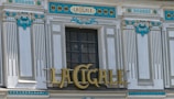 A decorative facade with ornate details features a central window surrounded by intricate patterns and carvings. The walls are adorned with blue and white elements, and a sign with gold lettering reads 'LA CIGALE'. The architectural style exudes a classic and artistic appeal.