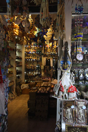 An indoor shop showcasing a variety of traditional and cultural items with intricate designs. The shelves are filled with decorative trinkets, including hanging ornaments, pottery, and figurines. The space is densely packed with colorful goods, creating a vibrant and eclectic atmosphere.