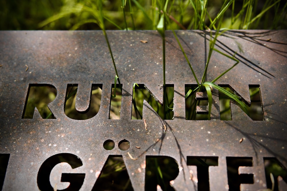 Un primer plano de un letrero de metal con hierba creciendo fuera de él