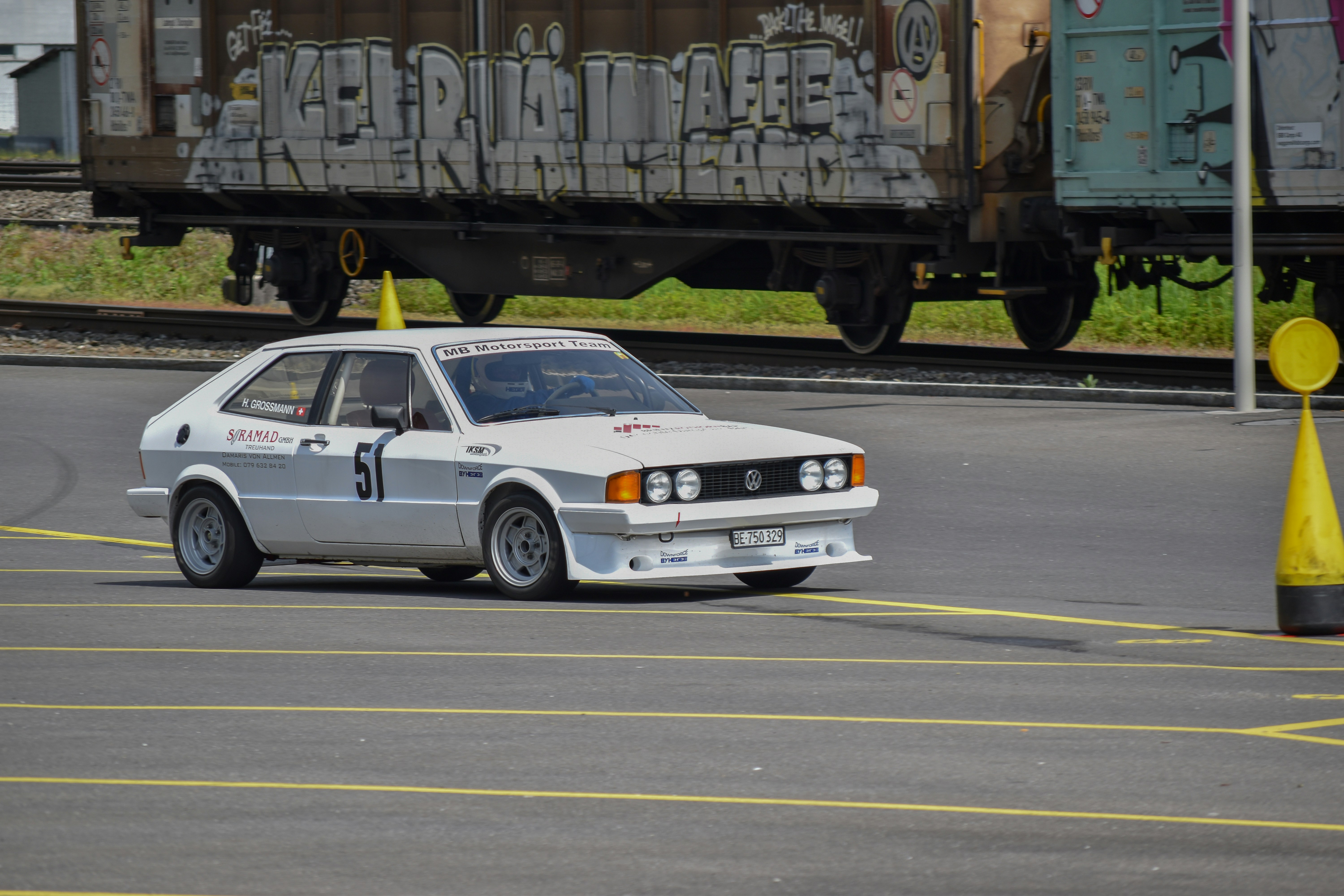 a white car driving down a street next to a train