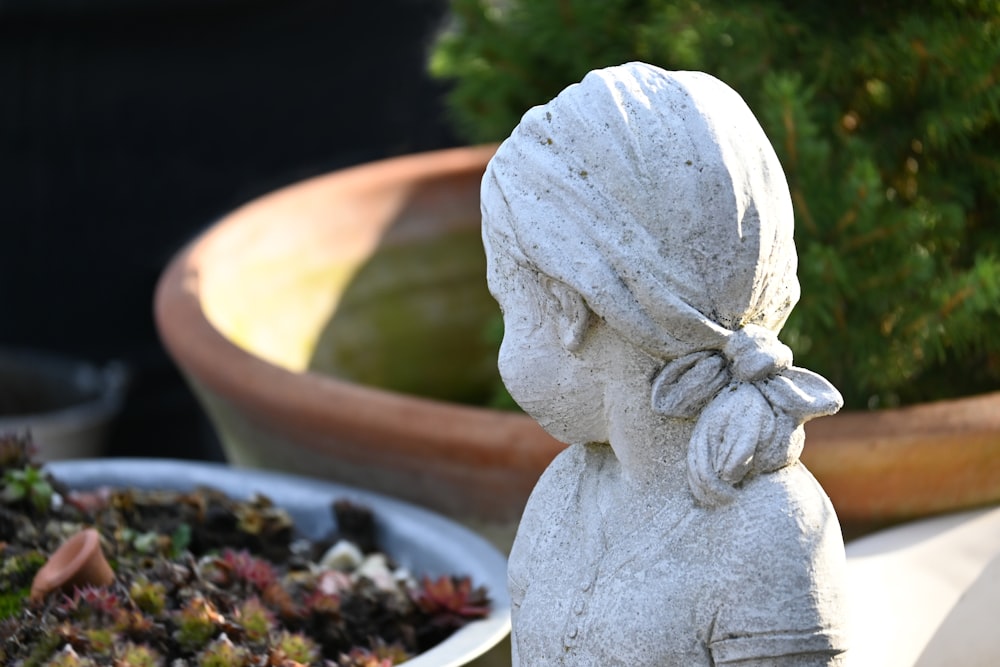 a statue of a little girl sitting next to a potted plant