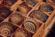 A collection of intricately designed ceramic bowls arranged in rows within cardboard packaging. Each bowl features detailed, symmetrical patterns in shades of black, tan, and white, creating an artistic and handcrafted appearance.