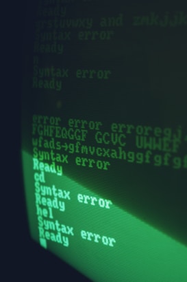 A computer screen displaying lines of text primarily consisting of 'Syntax error' messages in green monochrome. The text is written in a retro, pixelated font typical of older computer monitors.