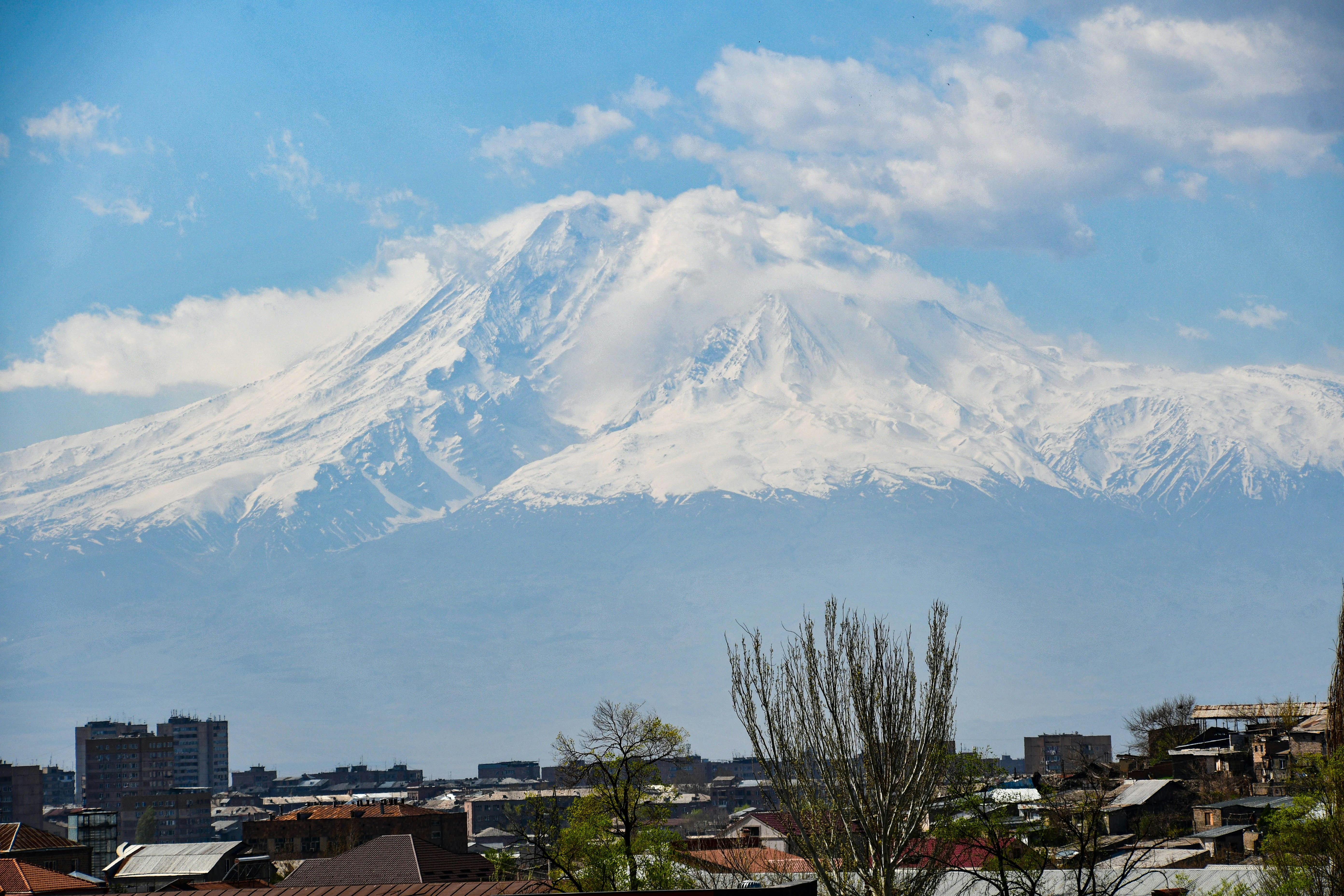 a large snow covered mountain towering over a city, 
