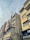 Tall, weathered buildings with prominent signs line a street that is covered by a web of overhead cables against a cloudy sky. The structures have signs like Hotel Al Haram and brands like Sony, indicating a mix of residential and commercial use.